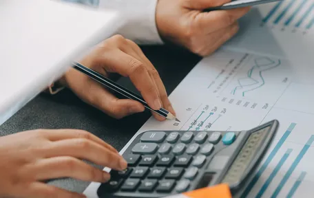 Varias manos trabajan con una calculadora, una tablet y planillas de gráficos