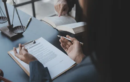 Una persona revisa un contrato en una tabla junto a un libro abierto y una balanza de la justicia