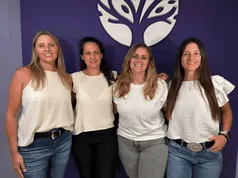 Cuatro integrantes del equipo frente al logo del árbol en la recepción