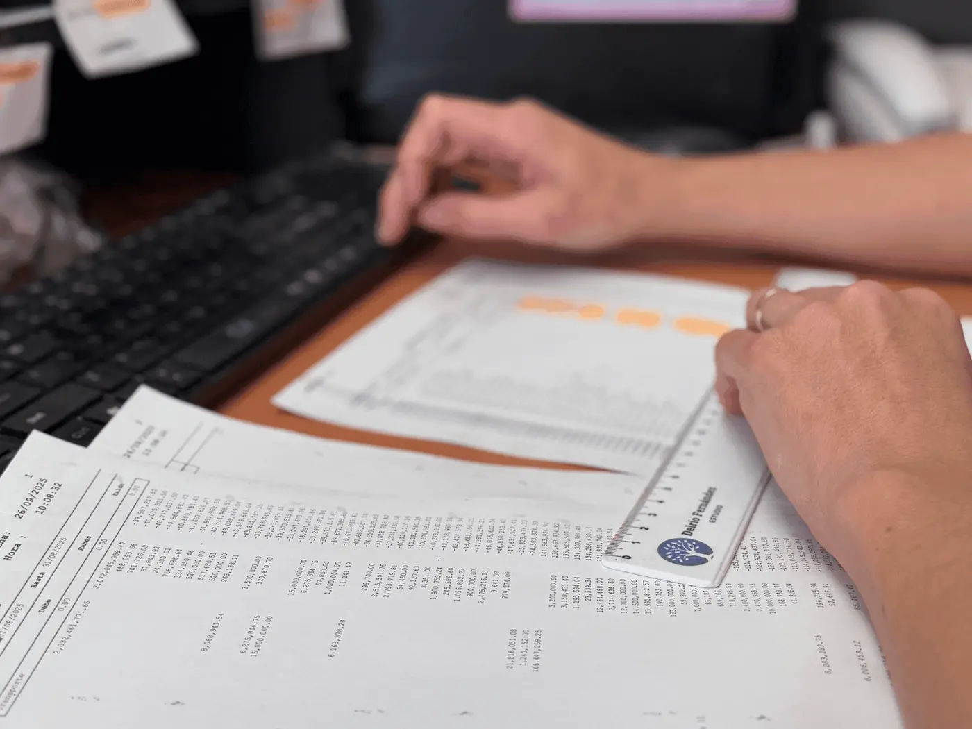 Manos revisando planillas impresas con una regla sobre el escritorio